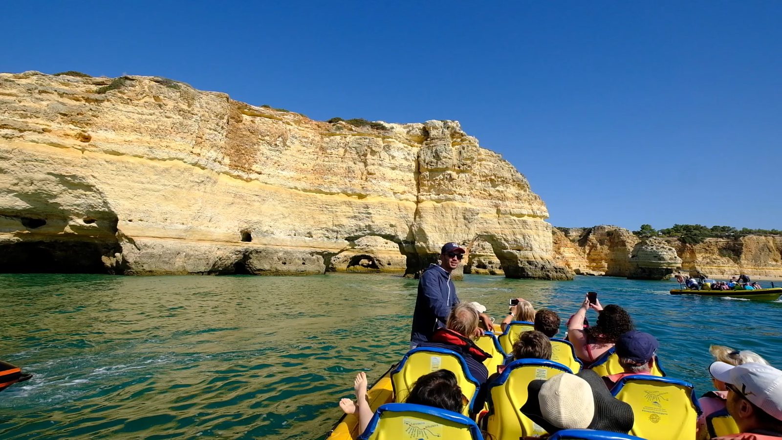 Guide talking to guests on a RIB speedboat beside the golden Algarve cliffs and sea caves